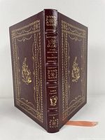 Front and back cover with spine of the burgundy leather bound book showing gold foil embossed illustrations and text