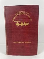 Front cover of the book showing red cloth with gilt lettering and a canoe design.