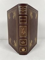 Front and spine view of the brown leather bound book with gold embossed details and titles: 'The Adventures of Huckleberry Finn', 'Mark Twain', 'The Franklin Library'.