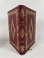 Front and back cover view showing maroon leather with gold gilded ornate decorations, title and author on spine, gold borders on cover.