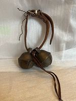 Photo showing pair of antique farm bells with leather straps standing upright on fabric backdrop.