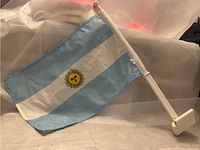 Small Argentine flag on white plastic pole designed to attach to car window.