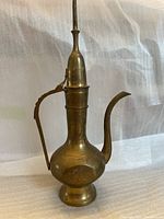 Front side view of the brass antique decorative pot showing curved handle and spout with engraved designs.