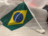 Brazil national flag attached to a white plastic pole and clip, designed for mounting on a car window.