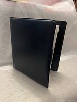 Closed black binder binder with a smooth finish seen from the front and slightly open showing the thickness