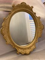Front view of the small oval mirror with ornate beige frame, showing clear glass surface and carved frame details.