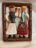 Front view of rectangular ceramic sculpture depicting traditional Hungarian dressed figures, glazed with brown frame and detailed coloring.