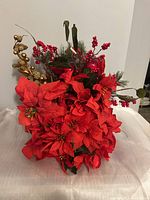 Front and angled views of the faux Christmas bouquet showing red poinsettias, red berries, gold decorative elements, and green foliage.