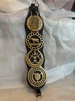 Full view of antique decoration piece showing leather backing and four brass medallions with Guernsey farm motifs.