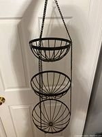 Front view of the metal triple holder showing the three circular basket tiers hung vertically by chains.