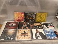 Overview of all 11 rap CD cases arranged in front of white fabric background showing front cover artwork and artist names.