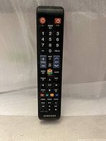 Samsung black TV remote control with numeric keys, volume, channel, color-coded buttons