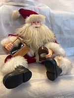 Front view of the Santa Claus figurine sitting, showing detailed beard, red outfit with white fur, holding a small wooden brush holder and a clock.