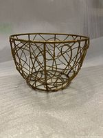 Front and side view of small round gold-toned metal wire basket holder showing abstract wire pattern