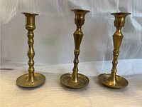 Front view of three brass candlestick holders of varying designs and sizes