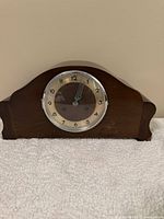 Front view of the wooden mantel clock showing the rounded top design and circular clock face with Arabic numerals and black hands under glass.