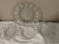 Photo of four clear glass plates: one large with scalloped edge and petal-like texture, three smaller plates with varied textured patterns and scalloped edges.