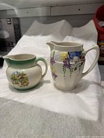 Two vintage ceramic milk creamers side by side, showing overall shape and floral designs