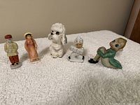 Five small Occupied Japan ceramic figurines arranged on white textured fabric, showing detailed designs and colors.