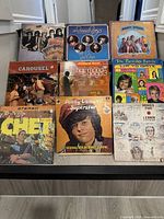 Photo showing nine vinyl record albums laid out on the floor. Albums include classic and oldies artists such as Travelling Wilburys, The Beach Boys, Donny Osmond, The Partridge Family, Chet Atkins and John Lennon.