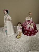 Photo of three Royal Doulton porcelain figurines including two adult females and one child with a dog.