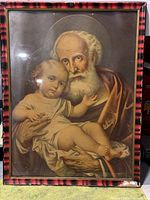 Frontal image of framed print showing older man with white beard holding young child, bordered with red and black colors.