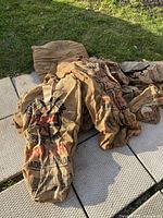 Photo showing a pile of burlap bags laid on a paved area outdoors with grass background. The bags have printed text and logos; some are plain. Condition appears good but used.