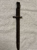 Single metal WWII dagger blade missing its handle, showing rust and patina on all metal surfaces