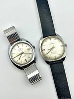 Two watches laid flat showing front dials and bracelets