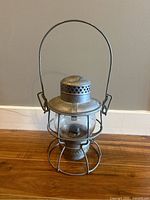 Full view of antique railroad lantern made of metal with glass globe and wire frame handle.