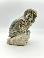 Side view of the carved soapstone owl showing detailed feather and facial carving, perched on a natural stone base.