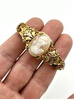 Close-up of the bracelet in hand showing carved shell cameo and ornate filigree band.