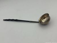 Full view of entire ladle showing silver bowl and twisted black balleen handle with metal collar at connection.