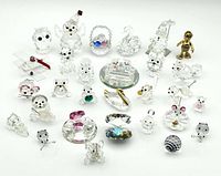Photo showing the complete set of 28 clear glass and crystal animal and object figurines arranged in white background, included are various animals, a snowman, plane, train, and objects with colored accents.
