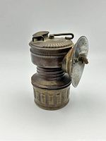 Front-side view of the lamp showing ribbed metallic body, hinged lid, and round reflector.