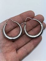 Photo showing the earrings held in hand for scale, visible dents and silver texture.