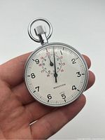 Front view held in hand showing white dial with black numerals 1-12 and red numerals 13-24, MARATHON brand, and stopwatch crown with loops on top