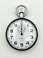 Front-facing photo showing the white dial with black Arabic numerals, smaller subdial with red marker, winding crown and ring attachment.