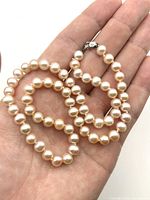 Close-up image showing the peach pearl beads and the silver clasp held in a hand for scale, highlighting the pearl size and luster.