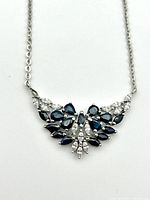 Front view of the necklace showing the detailed V-shaped pendant design with natural blue sapphires and clear crystals set in silver.