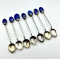 Seven silver teaspoons with twisted stems and oval lapis lazuli handles arranged in a row showing overall condition and materials.