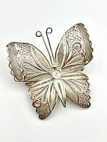 Top down view of sterling silver butterfly brooch showing detailed filigree and raised circular designs on wings.