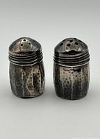 Pair of small sterling silver salt and pepper shakers with visible wear and patina.