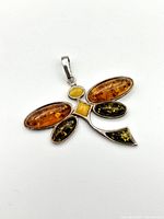 Close-up front view of the sterling silver dragonfly pendant with amber stones laid flat showing stone colors and settings.