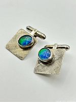 Pair of sterling silver cufflinks with oval opal stones on textured rectangular bases shown on white background.