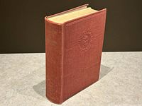 Red hardcover book standing upright, showing spine with gold embossed title and noticeable edge wear.