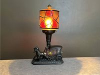 Lit view of the Art Deco stagecoach lamp showing the glowing stained glass shade with warm colors.