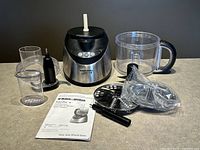 Full contents shown including food processor motor base, main bowl with handle, multiple discs, accessories, and instruction manual arranged on a table.