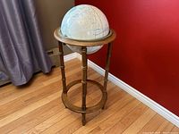 Full view of the globe on wooden stand with four legs and circular base against red background and curtain.