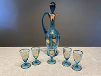 Full view of the blue glass decanter with stopper and five matching cordial glasses arranged in front of it.